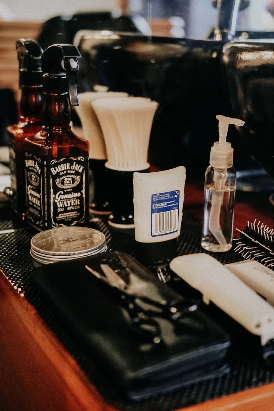 A barber's counter with spray bottles, shaving brushes, a tin of pomade, a pump bottle and a scissors case