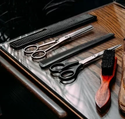 Scissors, thinning shears, black combs and a small brush laid out on a polished wooden counter