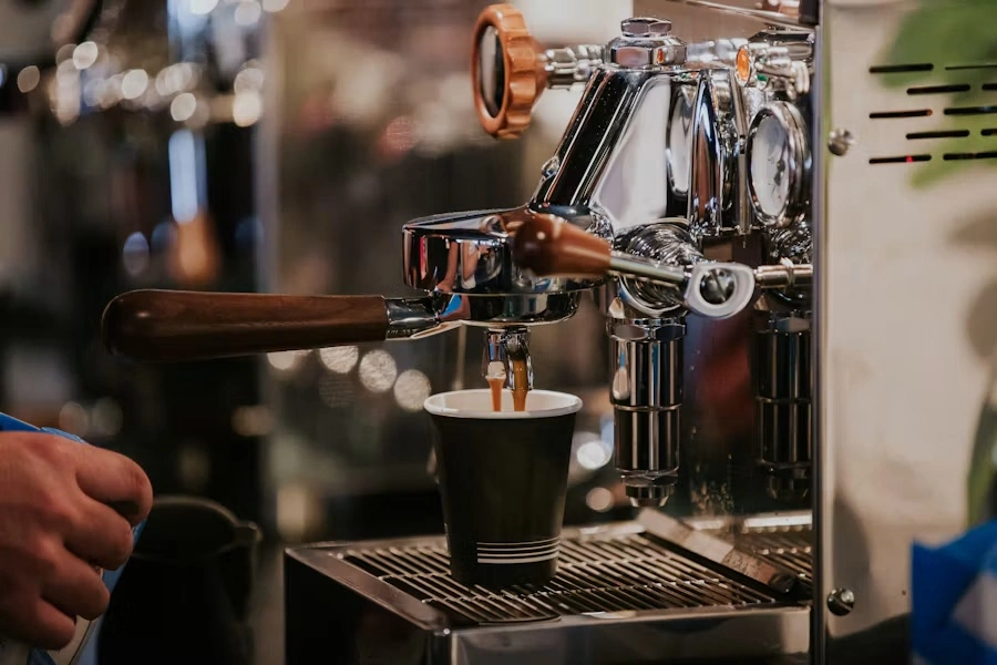 Espresso pouring from a chrome machine into a black paper cup
