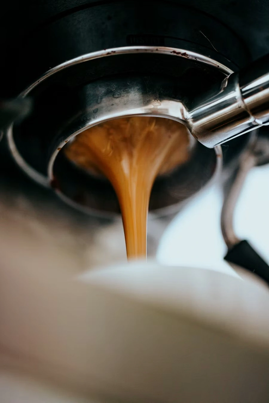 Close-up of espresso pouring from a portafilter spout into a cup