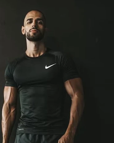 Coach in black training gear standing against a dark wall, upper body