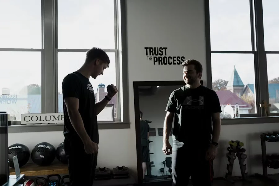 Two trainers talking in a bright gym beside a mirror and medicine balls