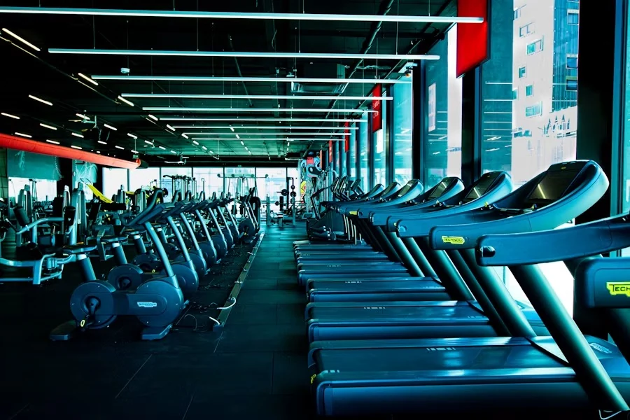 A long row of treadmills in a teal-lit cardio hall