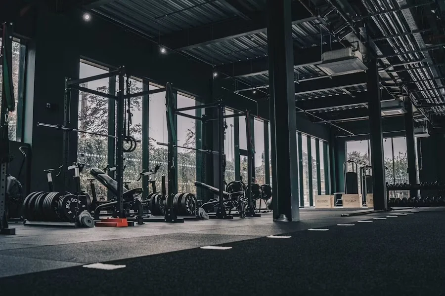 Wide view of a dark industrial gym floor with racks, plates and tall windows