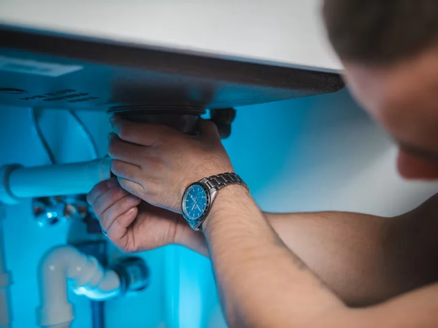 A plumber's hand with a wristwatch tightening a pipe fitting under a sink, lit in blue