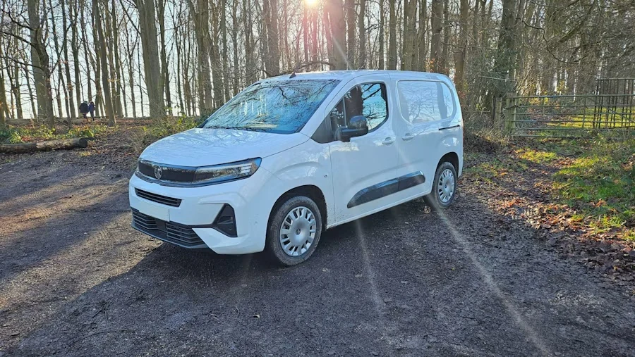 A white work van parked on a dirt track in a sunlit wood
