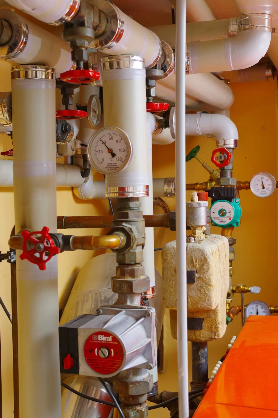 Boiler room pipework with white insulated pipes, red valve wheels and pressure gauges