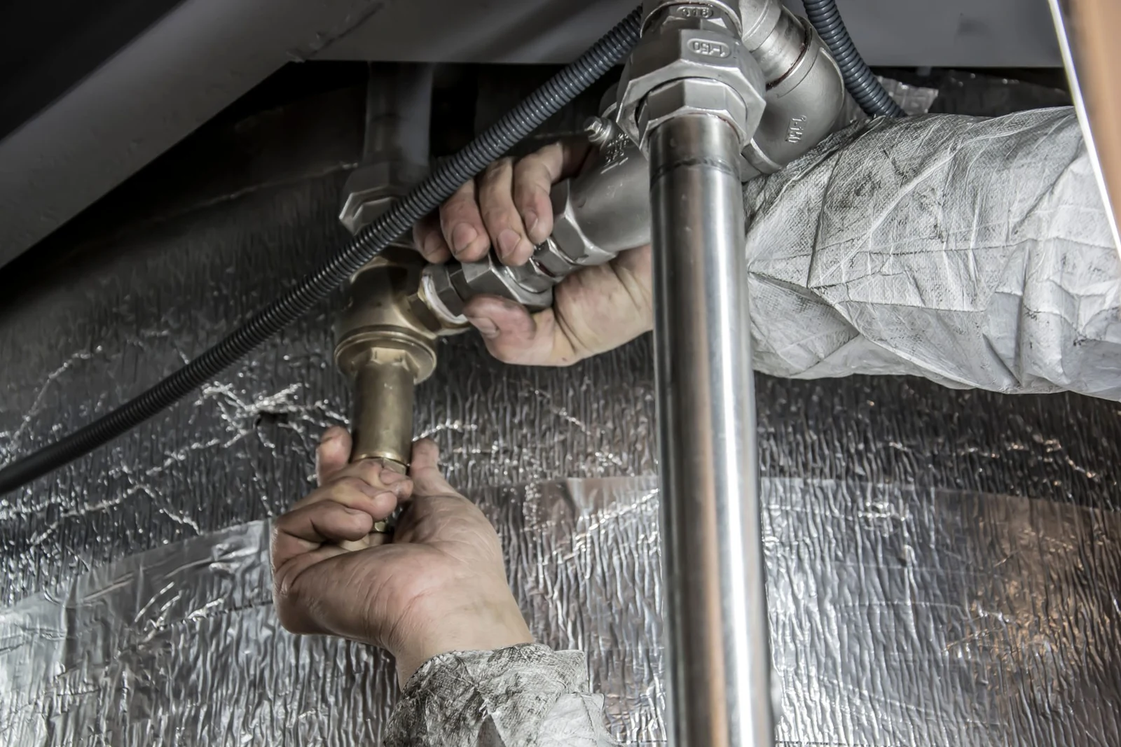 Hands tightening brass pipe fittings on insulated pipework
