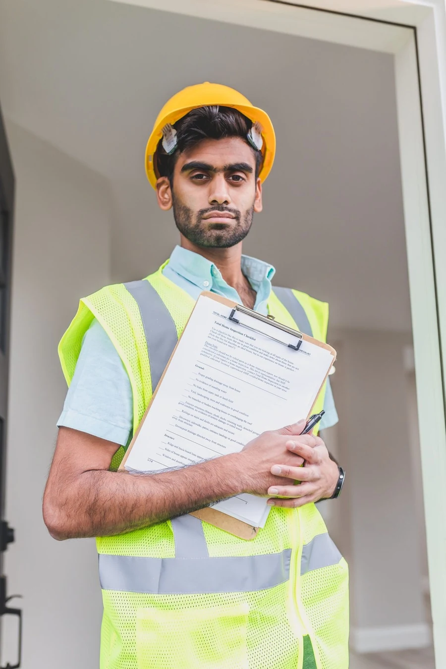 A plumber in a yellow hard hat and hi-vis vest holding a clipboard