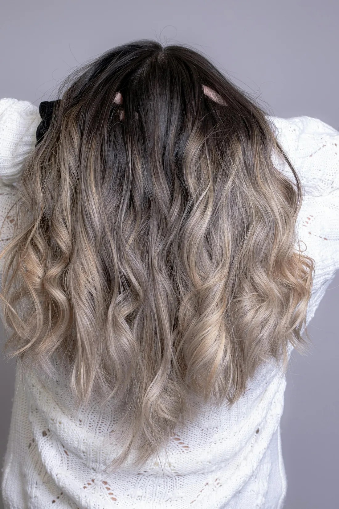 Back of wavy ash-blonde hair with a dark root