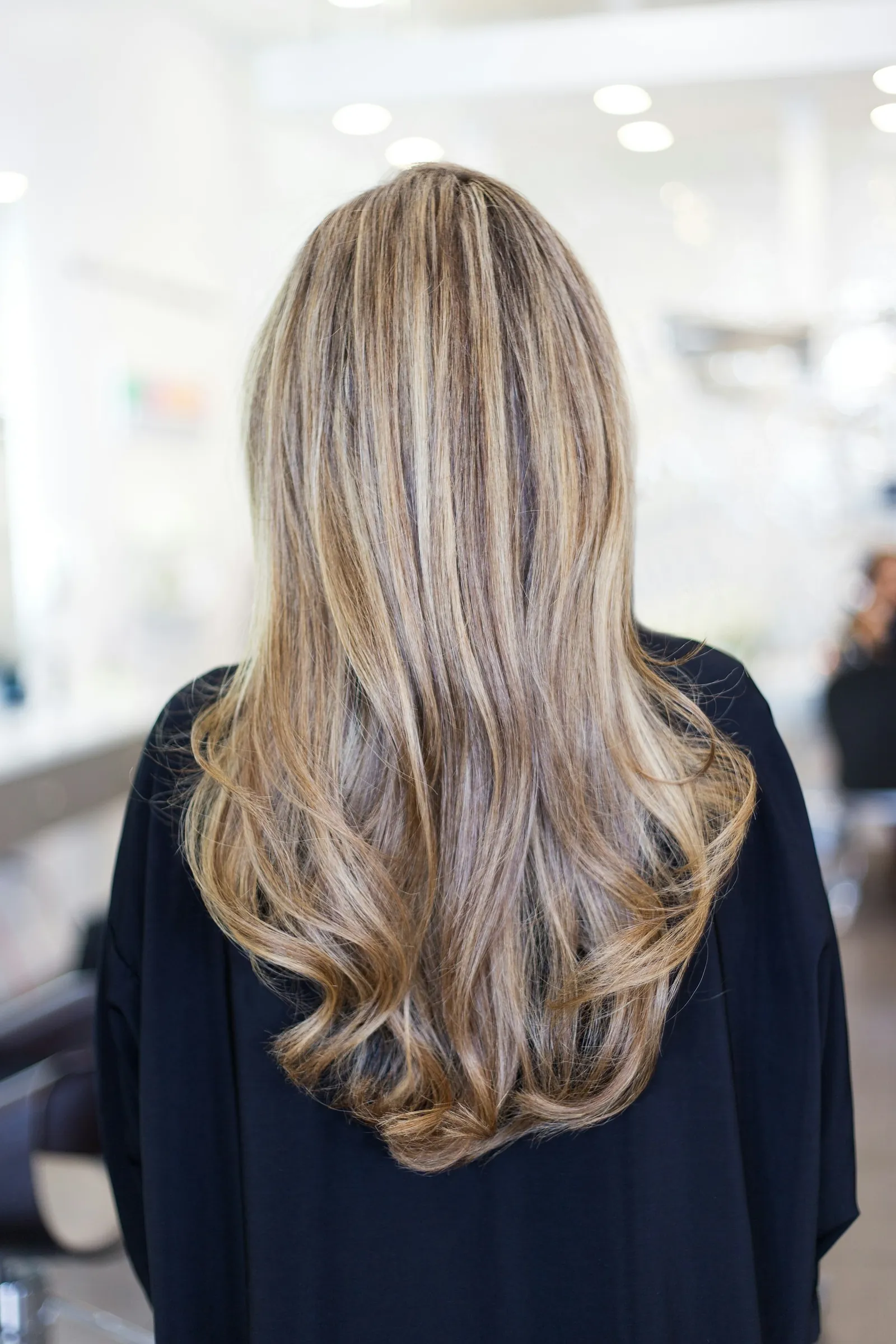 Back view of long, layered hair with blonde highlights in a bright salon