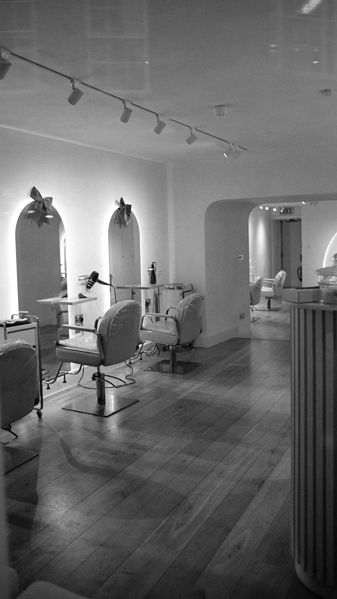 A black and white view of a calm salon with arched mirrors, chairs and track lighting
