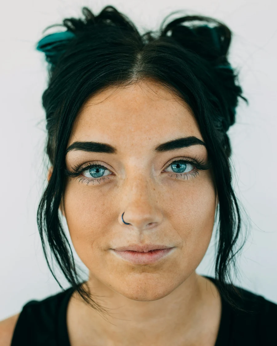 Portrait of a stylist with dark hair in two buns, blue eyes and a nose ring